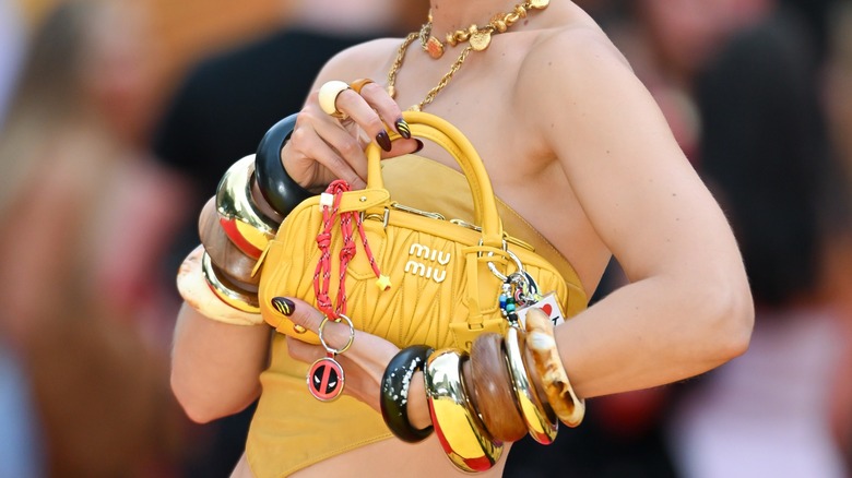 Gigi Hadid sosteniendo un Miu Miu amarillo con montones de brazaletes