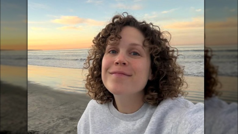 Erin Krakow posa para una selfie al amanecer en la playa mientras luce una sudadera gris y sus rizos naturales.