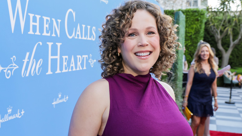 La actriz Erin Krakow aparece en la foto con el pelo rizado en la alfombra roja mientras lleva un vestido morado vibrante.