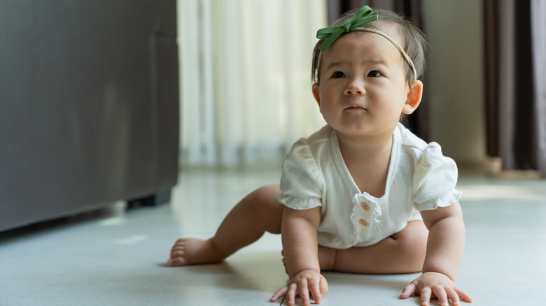 Un bebé gatea con una diadema y un mameluco blanco.