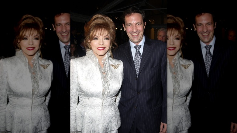 Joan Collins con un traje de falda blanca junto a Percy Gibson con traje