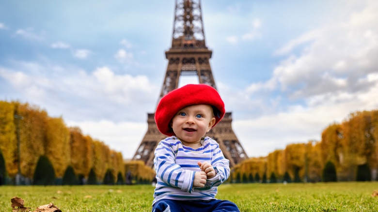 Un bebé con sombrero francés frente a la Torre Eiffel en París