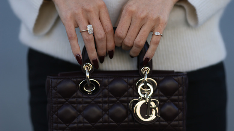 Una mujer con una manicura burdeos sosteniendo un bolso.