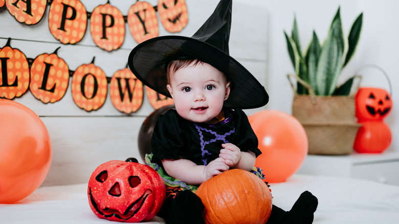 Un bebé disfrazado de bruja con decoración de calabazas.