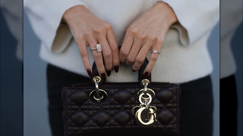 Una mujer con uñas de color rojo vino oscuro sosteniendo un bolso.